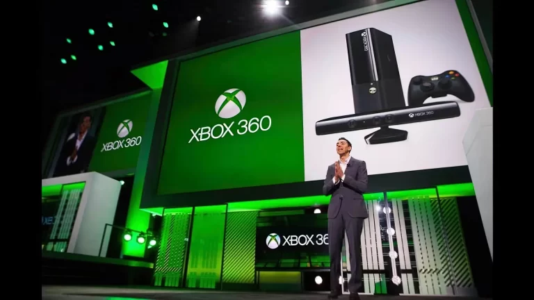 A person is standing on a stage in front of multiple large screens displaying the Xbox 360 logo and images of an Xbox 360 console and Kinect sensor.