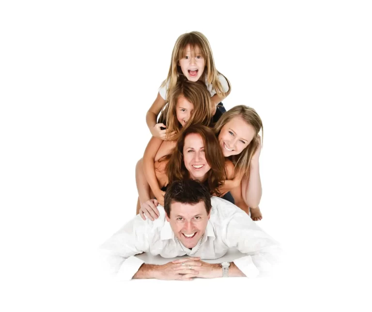Group of four people, consisting of a man lying on the floor with three children piled on top of his back, all smiling and posing for the camera.