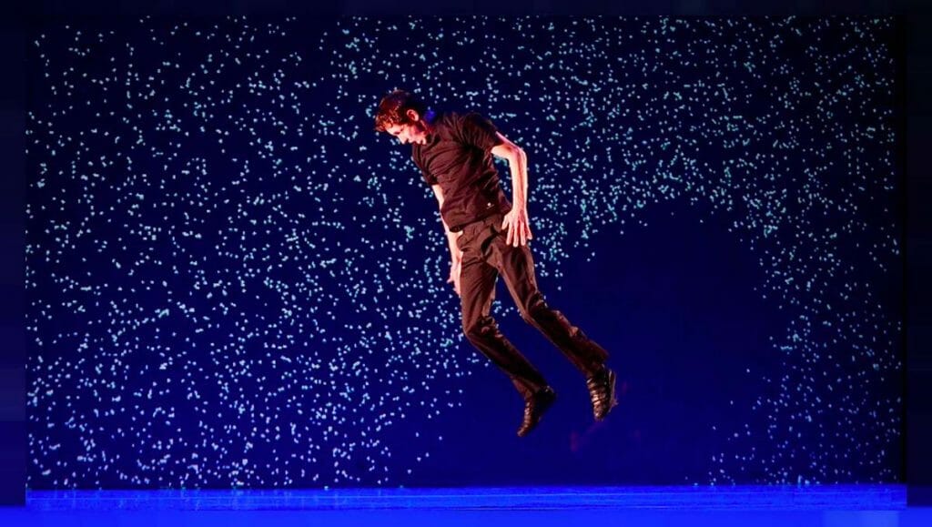 A man in black jumps in the air on a stage.