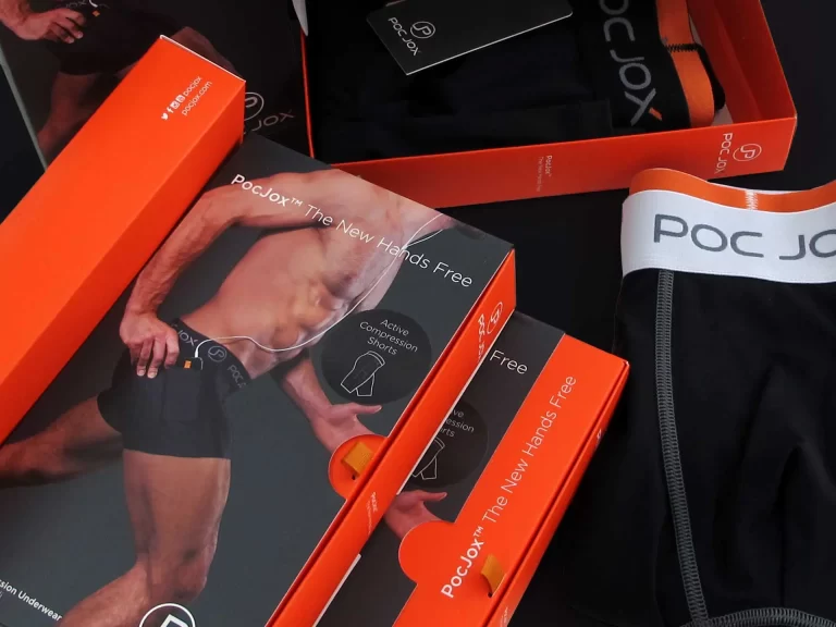 Close-up of packaging boxes for black underwear from the brand "PocJox," featuring images of the product and a model, all with orange accents and branding.