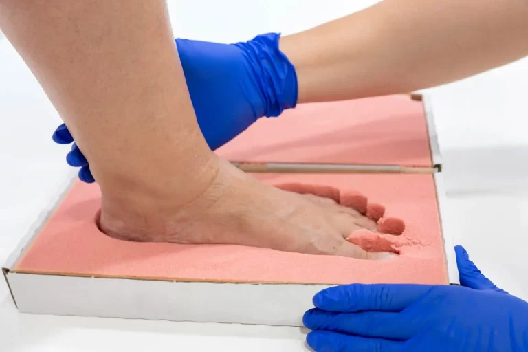 A foot is being pressed into a pink mold by hands wearing blue gloves.