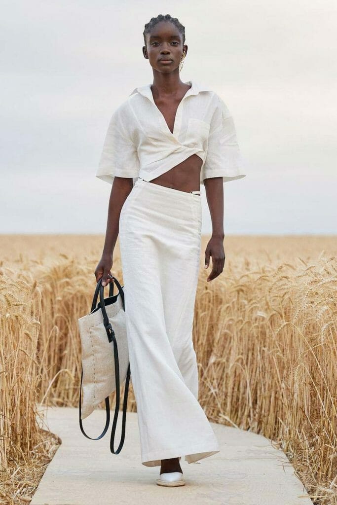 A woman in a white dress walks through a wheat field.