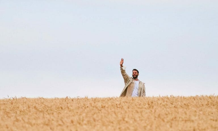 A man standing in a wheat field waving his arms.