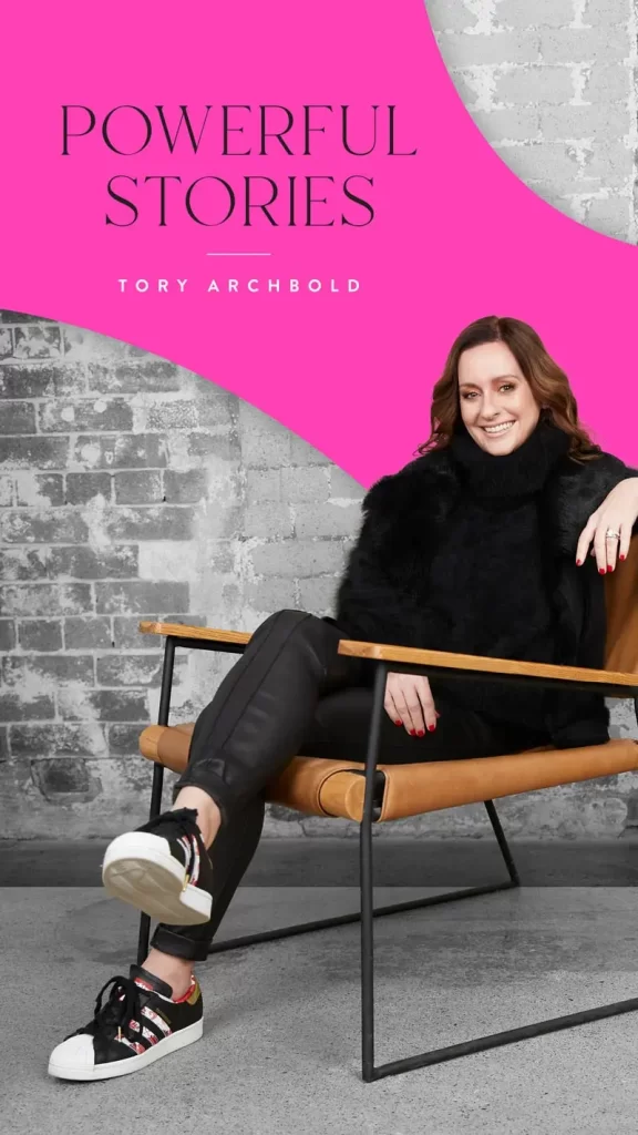 A seated individual in a black outfit and Adidas sneakers, smiles in front of a gray brick wall. Text reads "Powerful Stories, Tory Archbold" on a pink background.