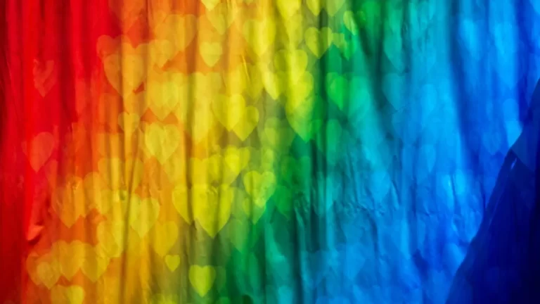 A colorful background displays a gradient of the rainbow transitioning from red to purple, with translucent heart shapes scattered throughout.