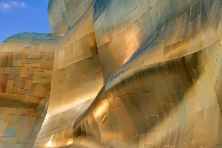 Close-up view of metallic building with abstract, curved and textured panels reflecting light.