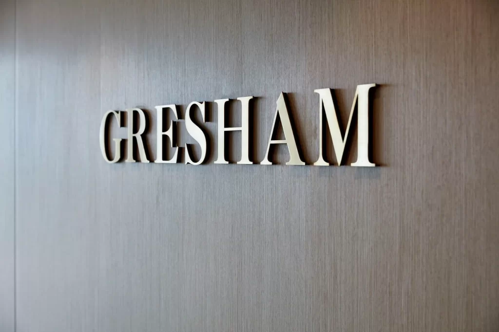 Close-up of the word 'GRESHAM' in large, metallic letters mounted on a wood-paneled wall.